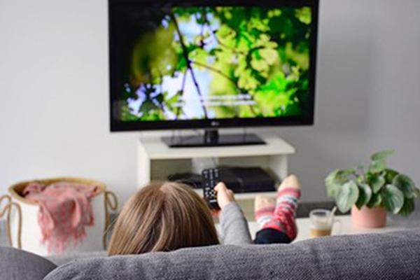 Female watching TV with captions while sitting on sofa in living room.
