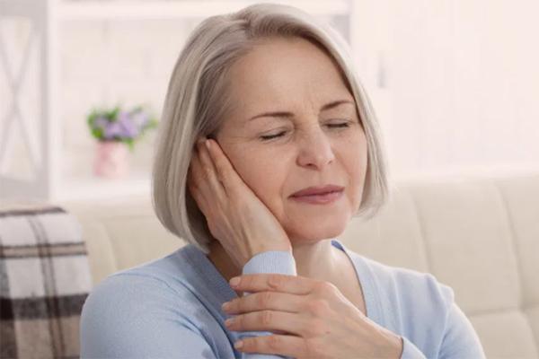 An old woman closing her eyes and holding her right ear with her right hand.
